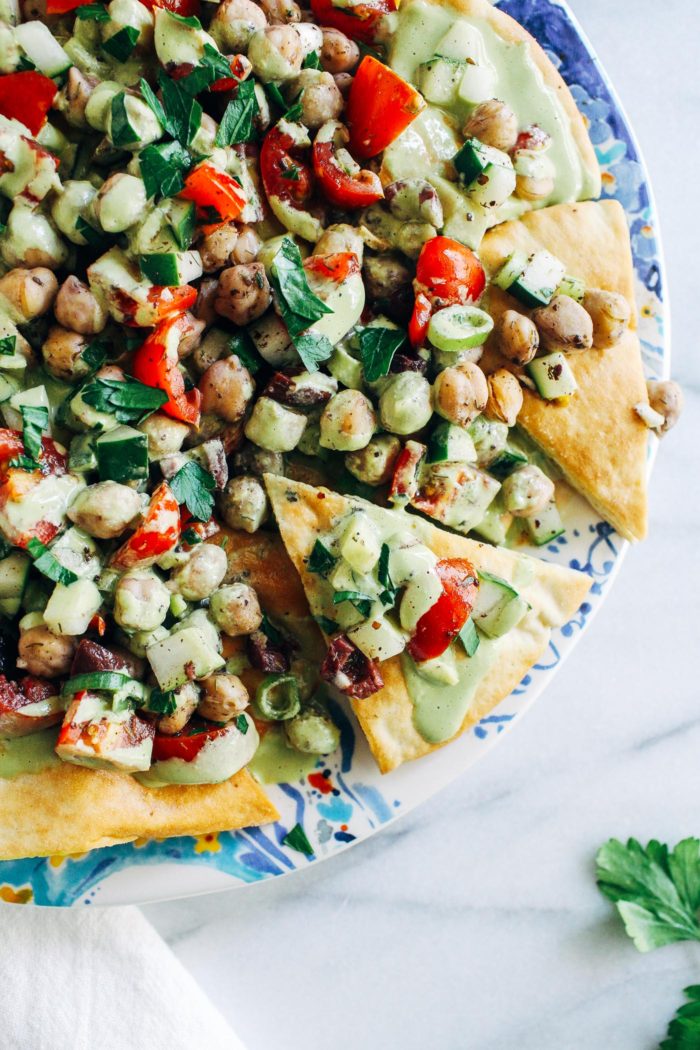 Fresh Greek Nachos with Herbed Tahini Sauce- toasted pita wedges topped with marinated Greek chickpea salad and a tangy herbed tahini sauce. No one will miss the cheese in these flavorful plant-based nachos! 