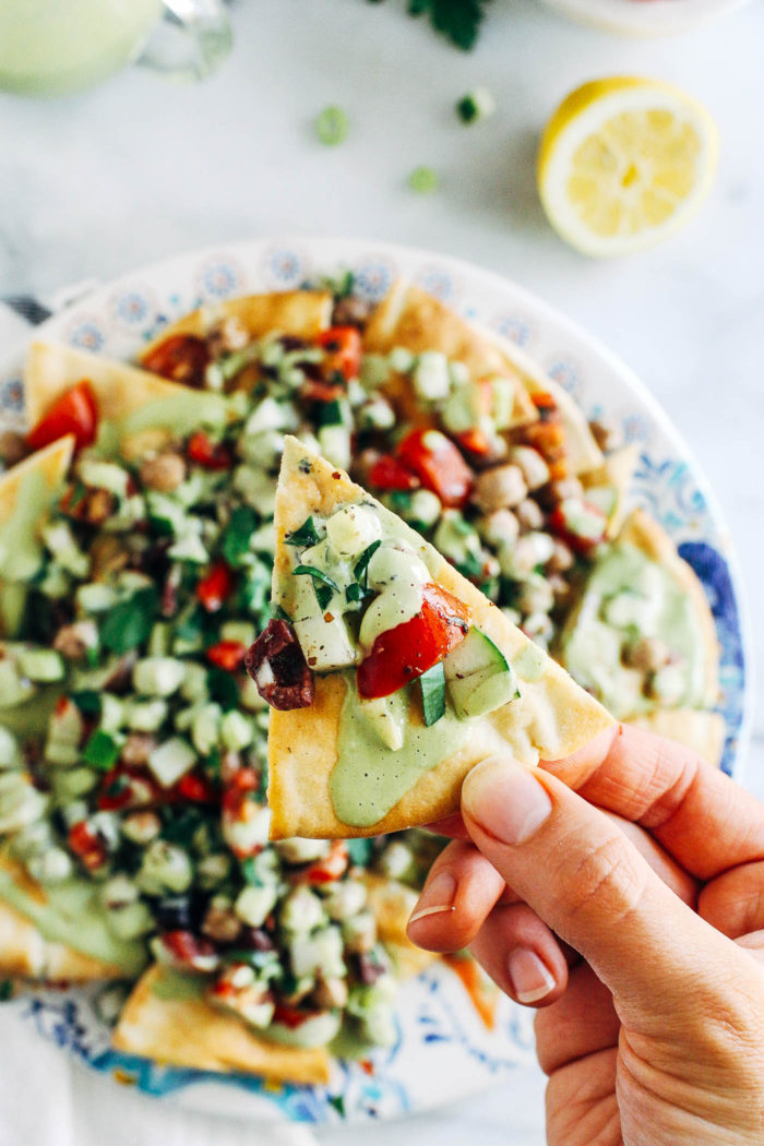 Fresh Greek Nachos with Herbed Tahini Sauce- toasted pita wedges topped with marinated Greek chickpea salad and a tangy herbed tahini sauce. No one will miss the cheese in these flavorful plant-based nachos! 