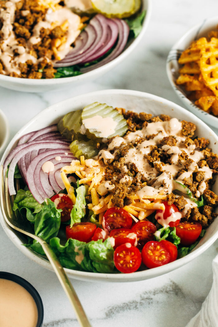 Vegan Burger Bowls- seasoned meatless grounds are served with crisp romaine and all of the best burger toppings plus a special sauce. Just 30-minutes to make and each bowl packs 27g of protein!