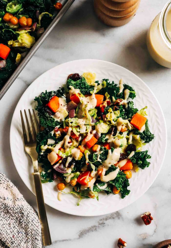Warm Kale Salad with Maple-Dijon Dressing- A colorful combination of roasted brussels sprouts, red onion, butternut squash and chickpeas served over a bed of kale with toasted pecans and tart dried cranberries. Packed with flavor and texture, this warm salad is sure to leave you craving more!
