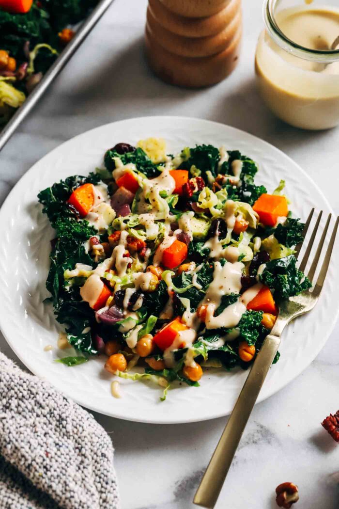 Warm Kale Salad with Maple-Dijon Dressing- A colorful combination of roasted brussels sprouts, red onion, butternut squash and chickpeas served over a bed of kale with toasted pecans and tart dried cranberries. Packed with flavor and texture, this warm salad is sure to leave you craving more!