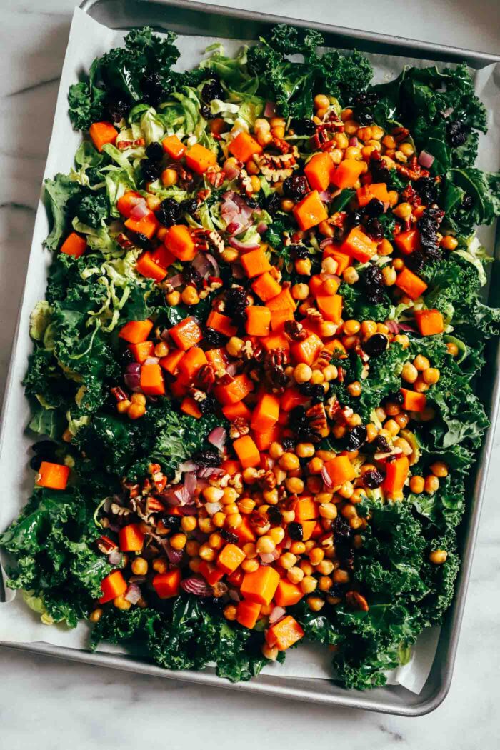 Warm Kale Salad with Maple-Dijon Dressing- A colorful combination of roasted brussels sprouts, red onion, butternut squash and chickpeas served over a bed of kale with toasted pecans and tart dried cranberries. Packed with flavor and texture, this warm salad is sure to leave you craving more!