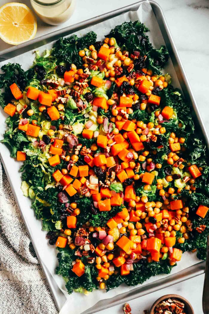 Warm Kale Salad with Maple-Dijon Dressing- A colorful combination of roasted brussels sprouts, red onion, butternut squash and chickpeas served over a bed of kale with toasted pecans and tart dried cranberries. Packed with flavor and texture, this warm salad is sure to leave you craving more!